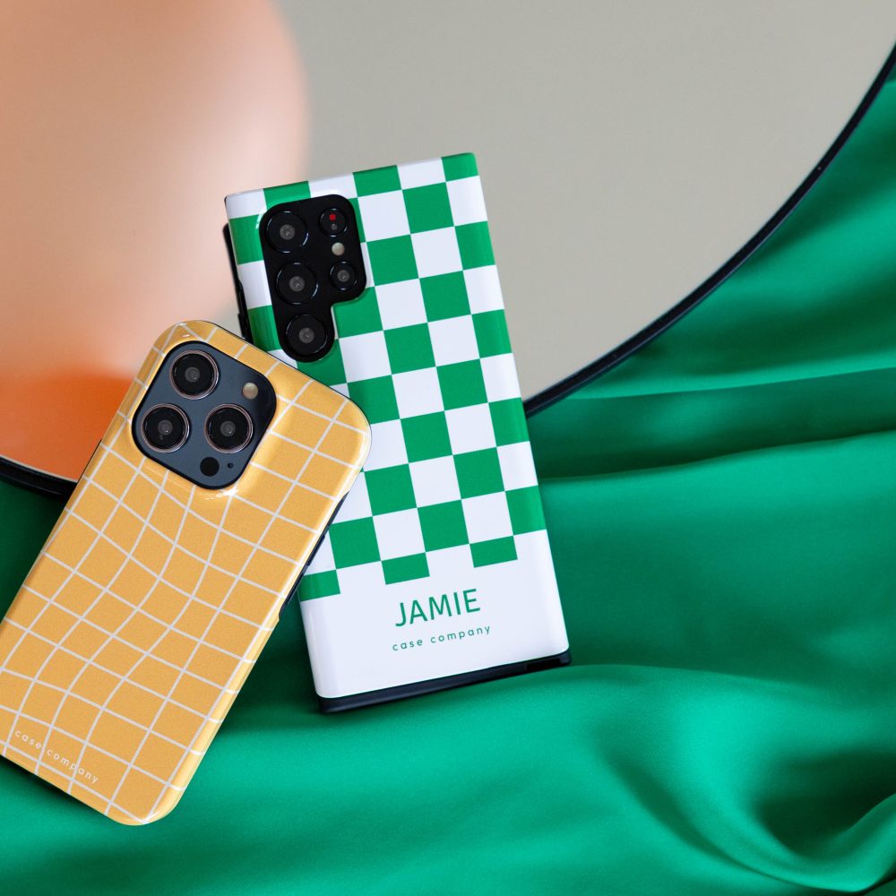 Két strapabíró tok: egy sárga kockás iPhone-hoz és egy zöld négyzetmintás, rajta a Jamie névvel